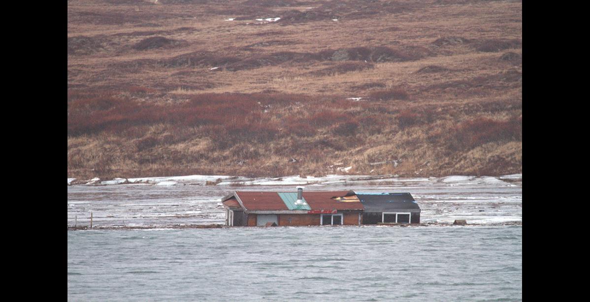 Photo by Jim Dory CABIN ADRIFT – Rita Hukill’s cabin drifts in the Nome River after it was swept off the sandspit at Fort Davis.