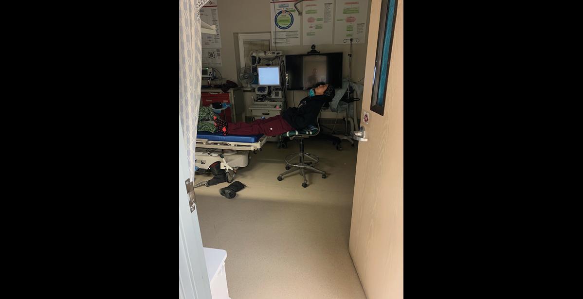 Photo by Mark Hayward EXHAUSTED—Michelle Tom, Stebbins community health aide level 3, is resting at a patient’s bedside after a 24-hour day doing COVID tests, contact tracing and responding to an overnight medical emergency.