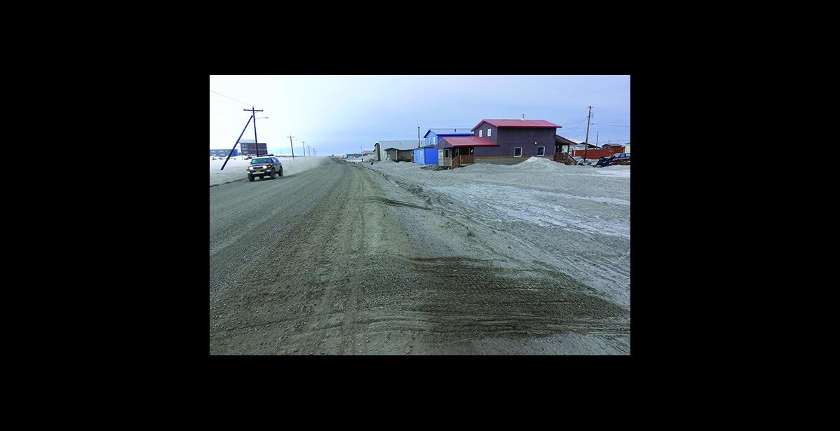 Photo by Nils Hahn DUST— A car kicks up dust on Greg Kruschek Avenue in ths photo taken at the end of April. Dark snow bears witness to the prevailing problem.