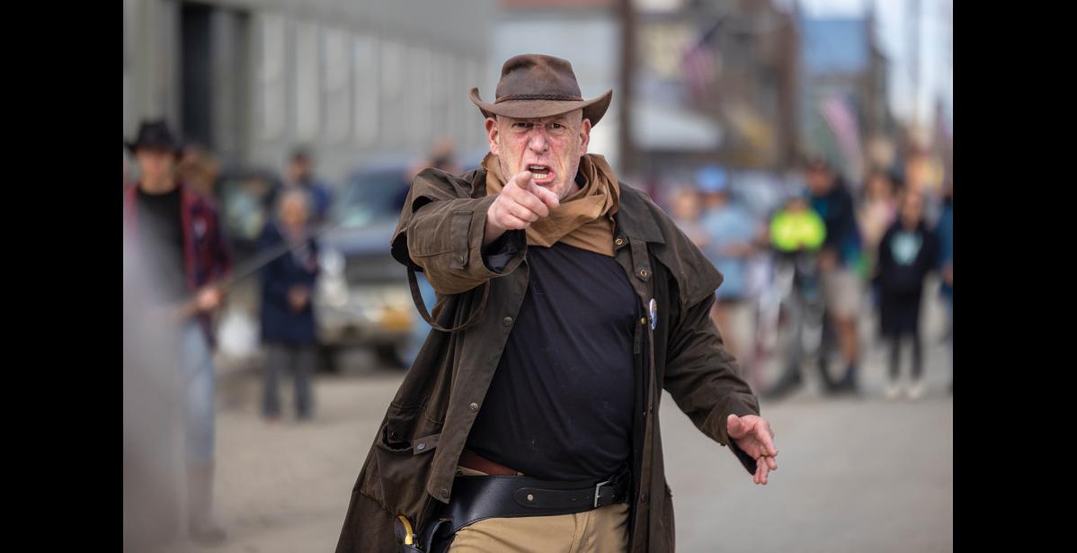 Photo by Sarah Manriquez First-time participant Tim Lowe, portraying the outlaw “Rubber Legs,” locks eyes with the crowd during the bank robbery reenactment at Nome’s Midnight Sun Festival on Saturday, June 21, 2025. Outfitted in his own costume and wielding a personal prop weapon, Lowe fully embraced his role as the second-in-command, intimidating bad guy. Energized by the crowd and festival spirit, he plans to return next year.