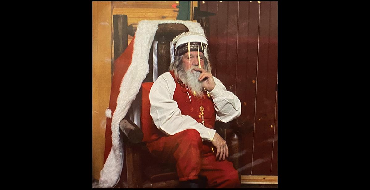 Photo courtesy Paul Kudla SANTA SOCIAL DISTANCES—While working as a professional Santa Claus in Anchorage, Nome’s Santa a.k.a. Paul Kudla must wear a face shield and sit behind a glass wall.