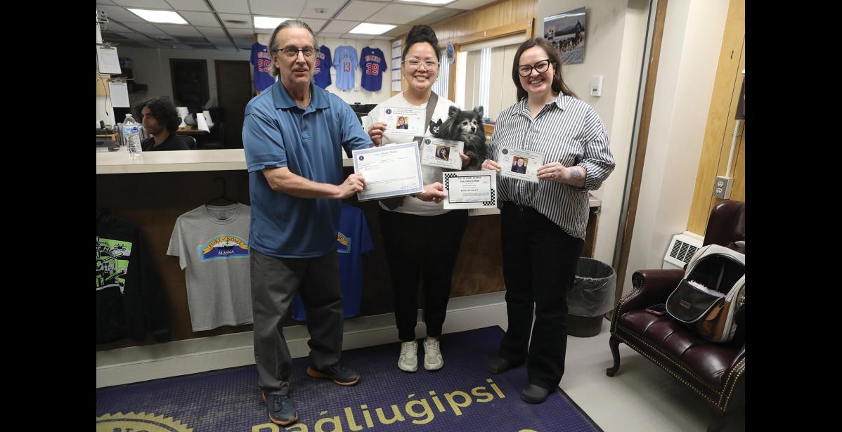 BOOTZ&CO CAB— Nome’s newest and only cab service is named after their dog Bootz, who also holds a chauffeur’s license. Here, City Clerk Brad Soske hands Billi Jean and Ashley Miller-Earp their business license, taxi registration and chauffeurs licenses, on Monday, July 6 at City Hall. Photo by Diana Haecker