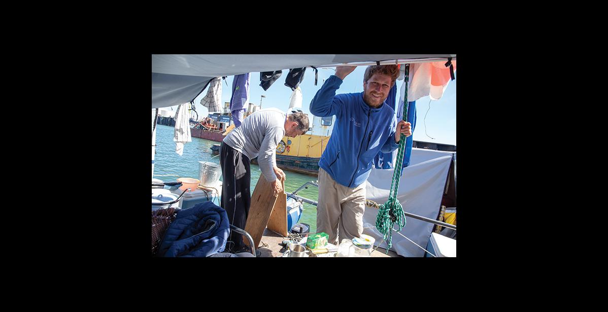Photo by James Mason ON BOARD— Alexander Lomb, left, works on a splash guard for their remaining Mercury outboard motor while Anatoli Kazakevich visits with the Nugget reporter. The Russians traveled from Lake Baikal to Nome in a catamaran and are currently en route to Dutch Harbor and on to Anchorage, their ultimate destination.