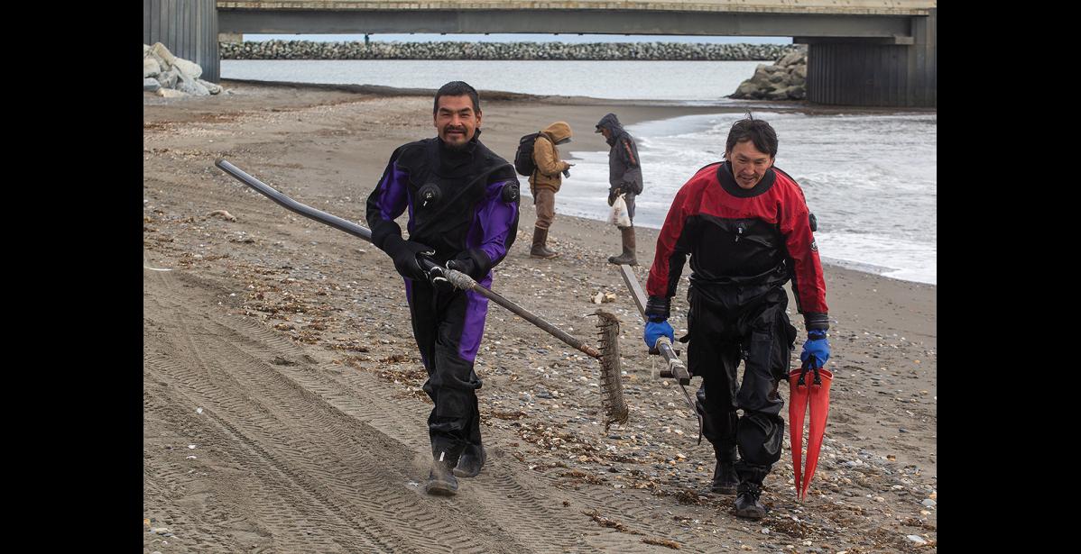Photo by James Mason SEARCHING FOR FLORENCE – SAR divers Tom and Joe Akeya of Savoonga walk up the beach after a day of diving off the causeway seawall at Nome’s West Beach. They assisted the search for Florence Okpealuk, who has last been seen on August 30 at West Beach